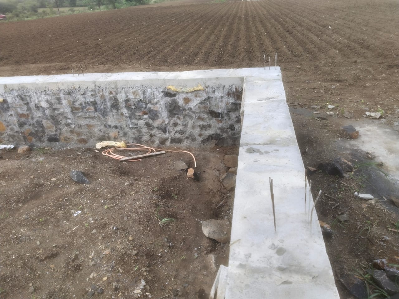 Stone retaining wall corner with concrete coping beside a field